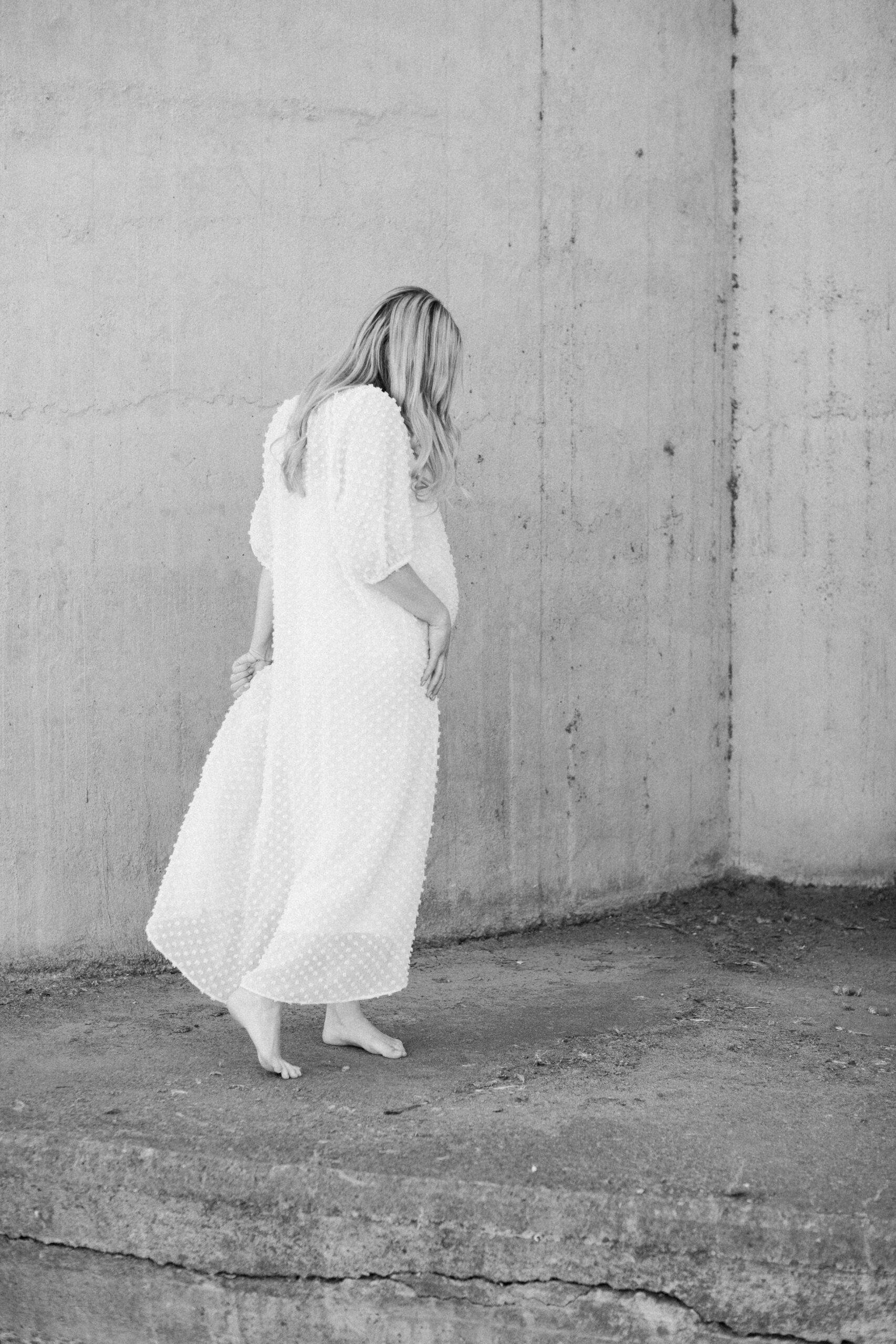 Gravidfotografering i Västerås med en kvinna som står på tå len lång vit klänning