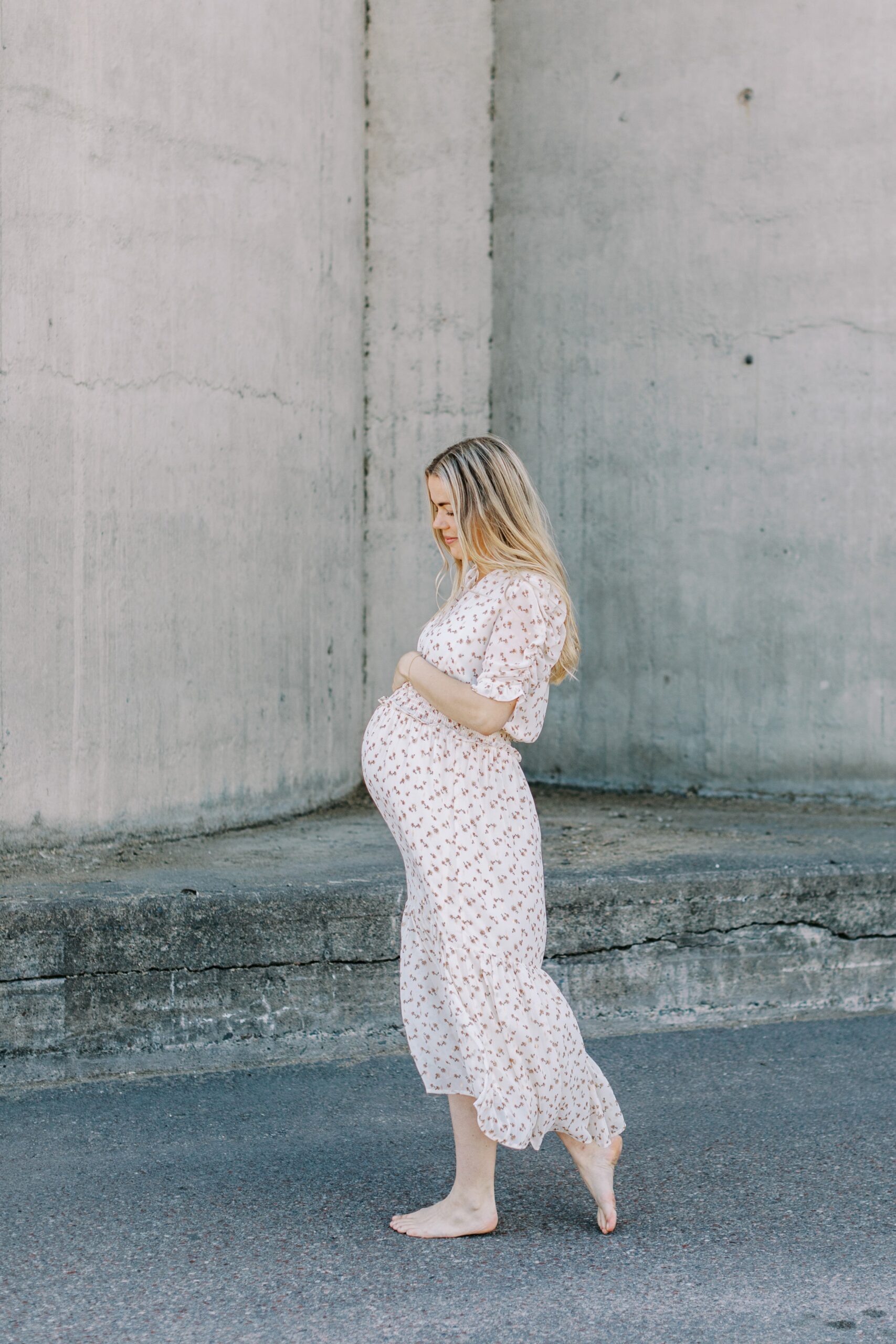 Gravidfotografering i Västerås där mamman går barfota i en lång blommig klänning
